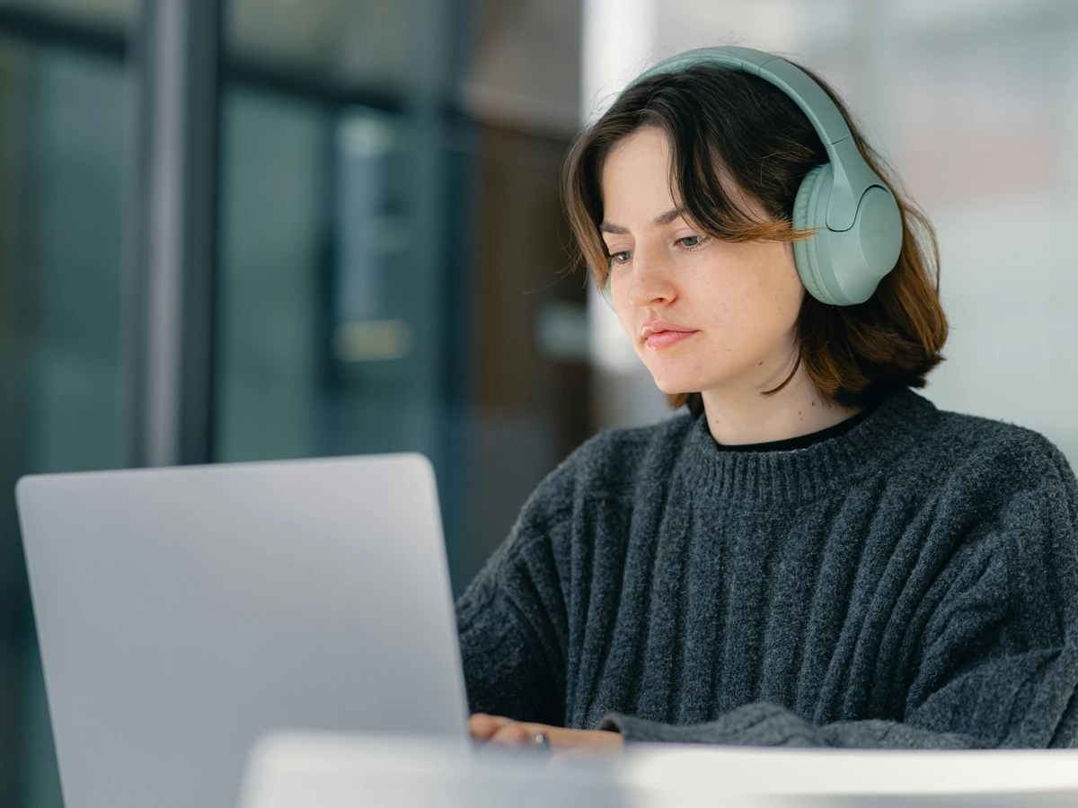 Young woman wearing headphones working at a laptop with focus and concentration