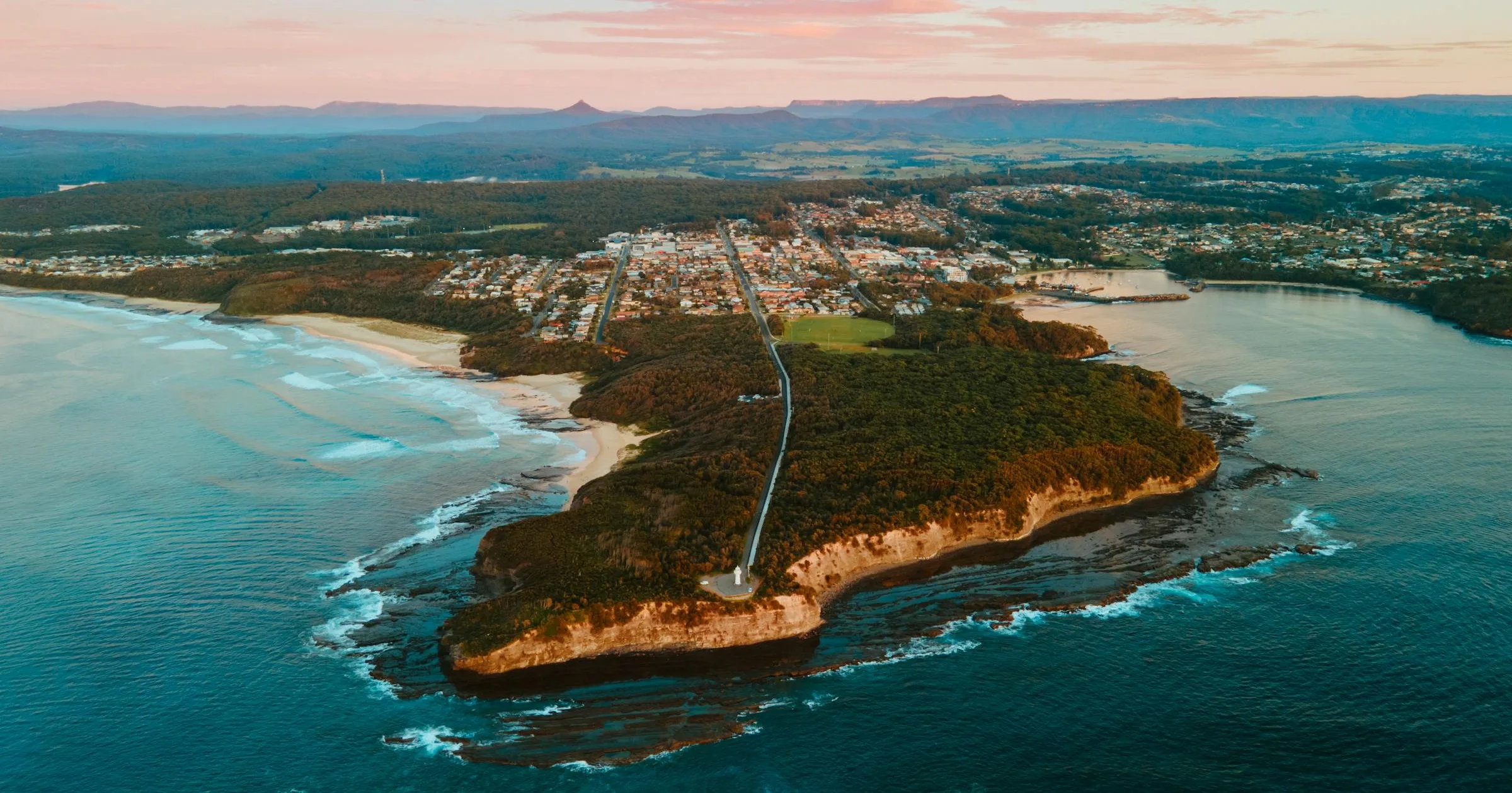 Aerial view of Ulladulla harbour and coastline at sunset with forest and town in regional New South Wales