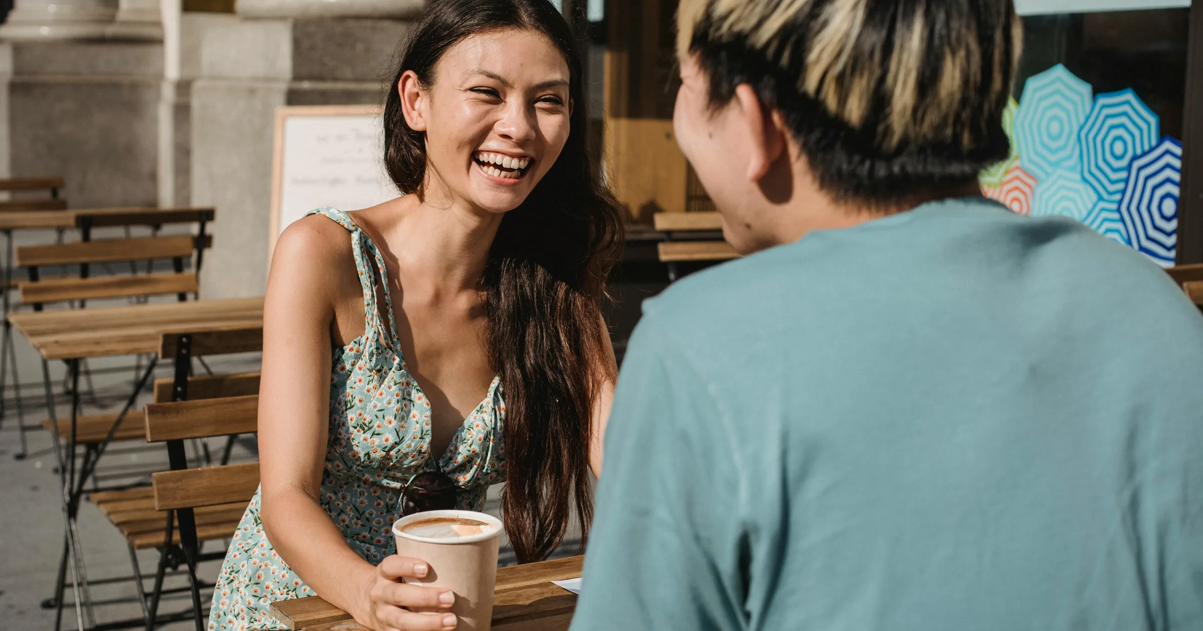 Two friends laughing over coffee at an outdoor cafe on a sunny day
