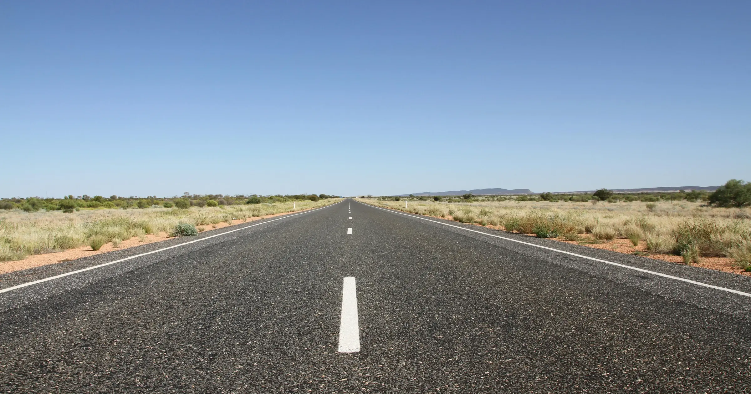Long straight road stretching through the Australian outback under a clear blue sky